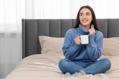 Photo of Happy young woman holding white ceramic mug on bed at home