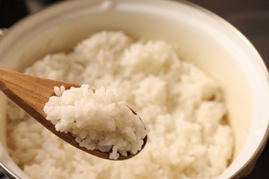 Wooden spoon with delicious rice over pot, closeup