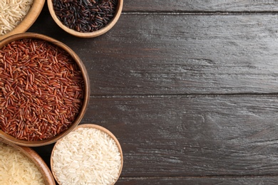 Photo of Flat lay composition with brown and other types of rice in bowls on wooden background. Space for text