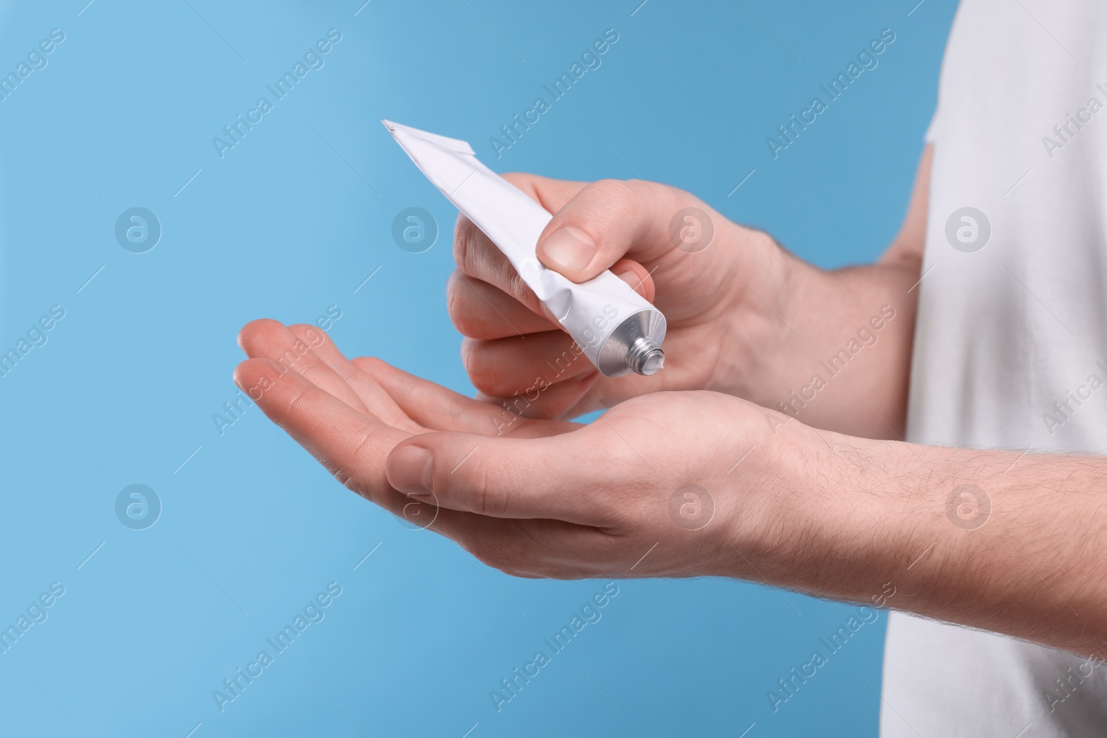 Photo of Man applying ointment from tube onto his hand on light blue background, closeup