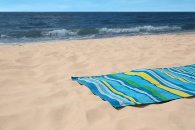 Photo of Bright striped beach towel on sandy seashore, space for text