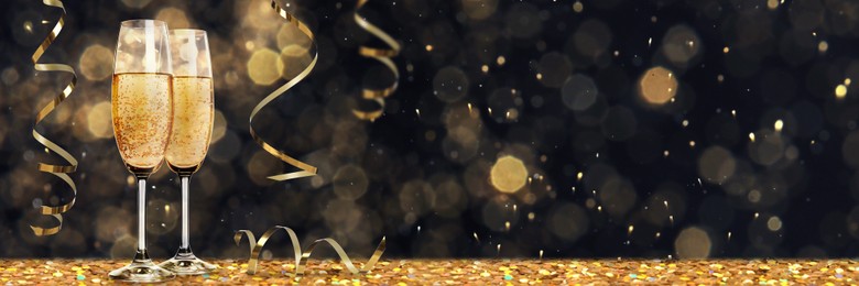Image of Glasses with sparkling wine and shiny serpentine streamers against blurred festive lights, space for text. Banner design