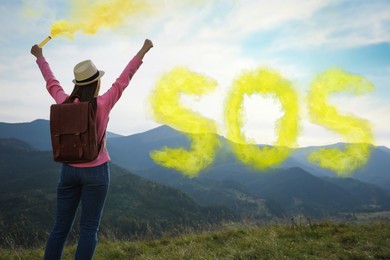 Woman with backpack and word SOS made of color smoke bomb in mountains, back view