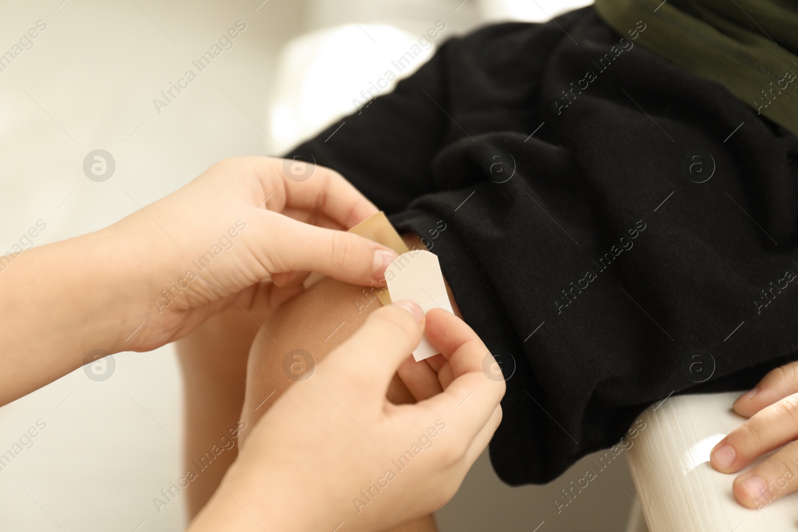 Photo of Sister putting sticking plaster onto little brother's leg indoors, closeup