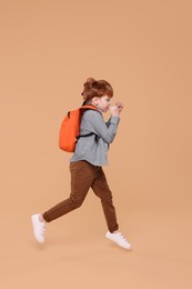 Photo of Cute schoolboy with backpack running on beige background