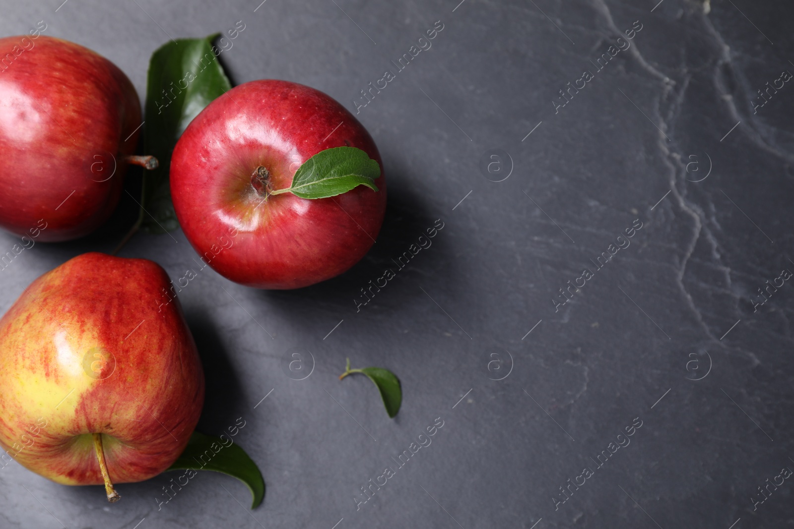 Photo of Ripe red apples and leaves on black textured table, flat lay. Space for text