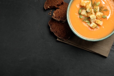 Delicious pumpkin soup in bowl on black table, top view. Space for text