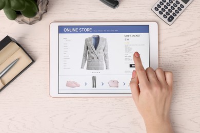 Woman with tablet shopping online at white wooden table, top view