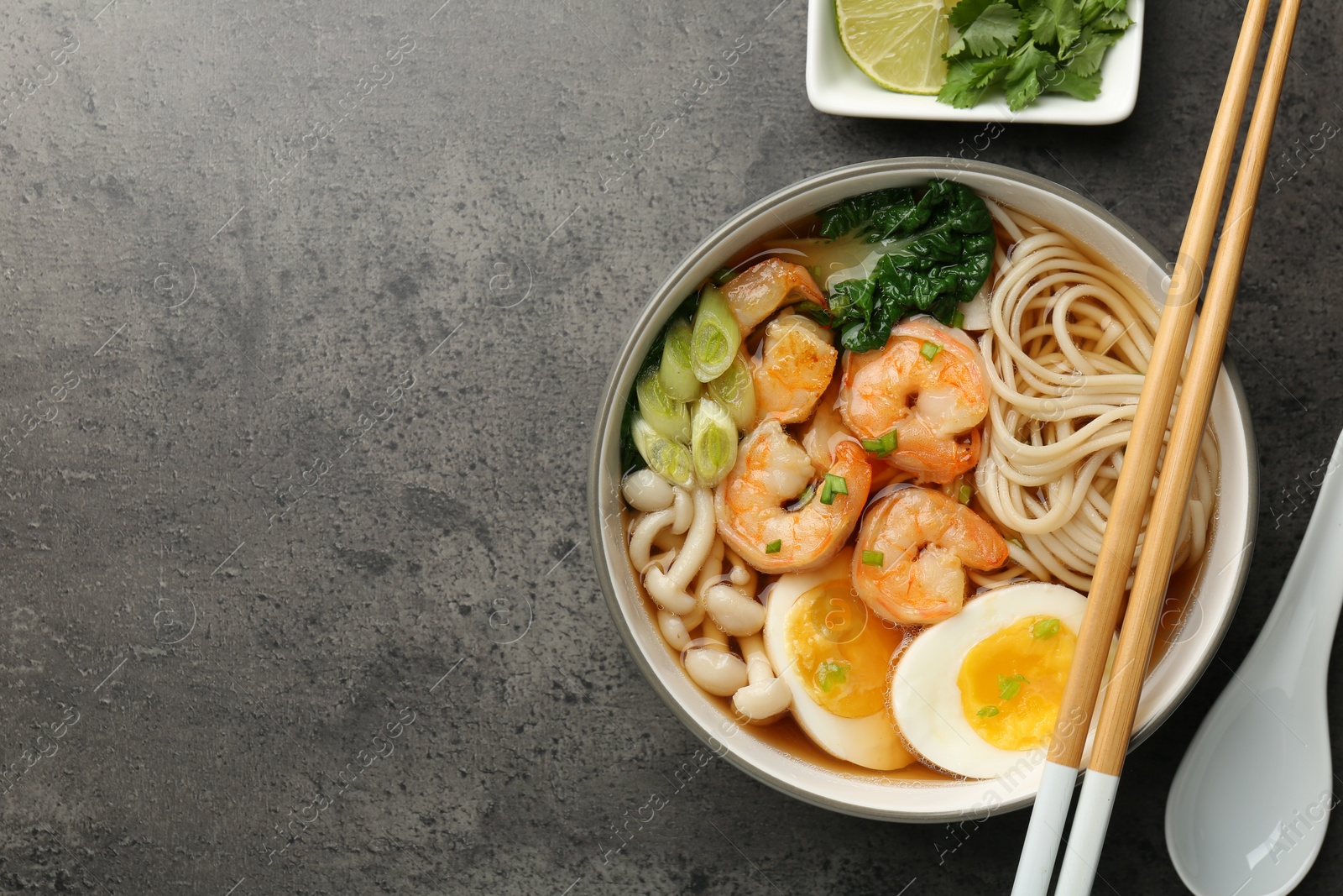 Photo of Delicious ramen with shrimps in bowl served on grey table, flat lay with space for text. Noodle soup