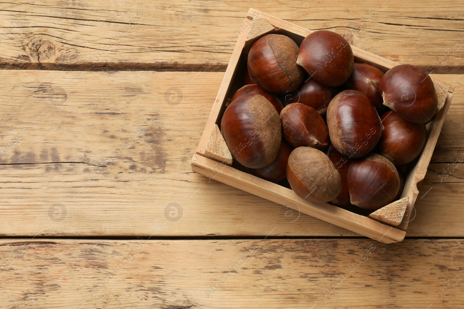 Photo of Sweet fresh edible chestnuts in crate on wooden table, top view. Space for text