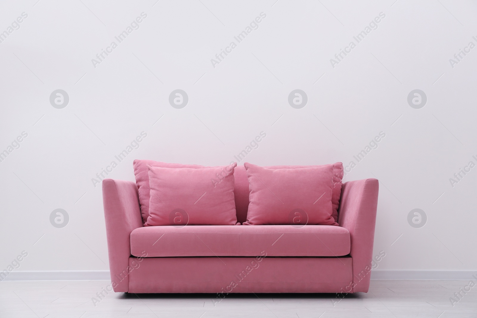 Photo of Comfortable pink sofa near white wall indoors, space for text. Simple interior