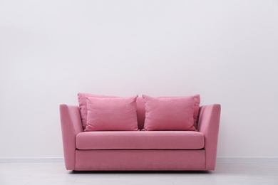 Comfortable pink sofa near white wall indoors, space for text. Simple interior