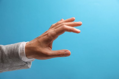 Man holding something in hand on light blue background, closeup. Space for text