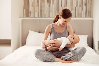 Young woman with her little baby resting after breast feeding in bedroom