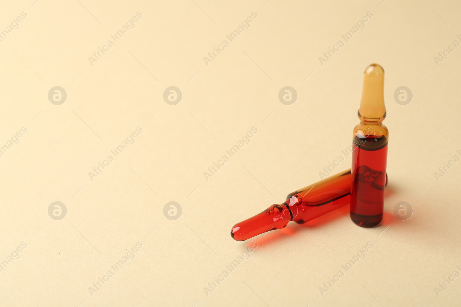 Photo of Glass ampoules with liquid on beige background. Space for text