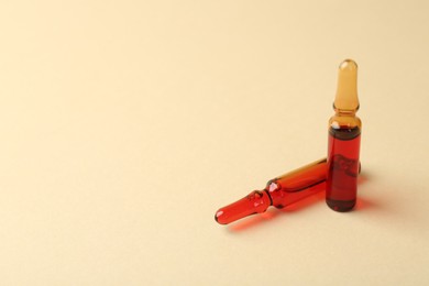 Photo of Glass ampoules with liquid on beige background. Space for text