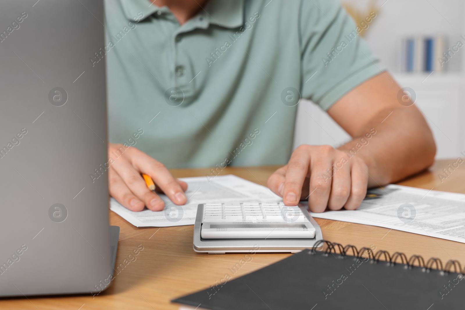 Photo of Man calculating taxes at wooden table in room, closeup