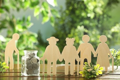 Pension savings. Figures of elderly people, coins in jar and green twigs on wooden table outdoors