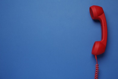 Photo of Red corded telephone handset on blue background, top view. Hotline concept