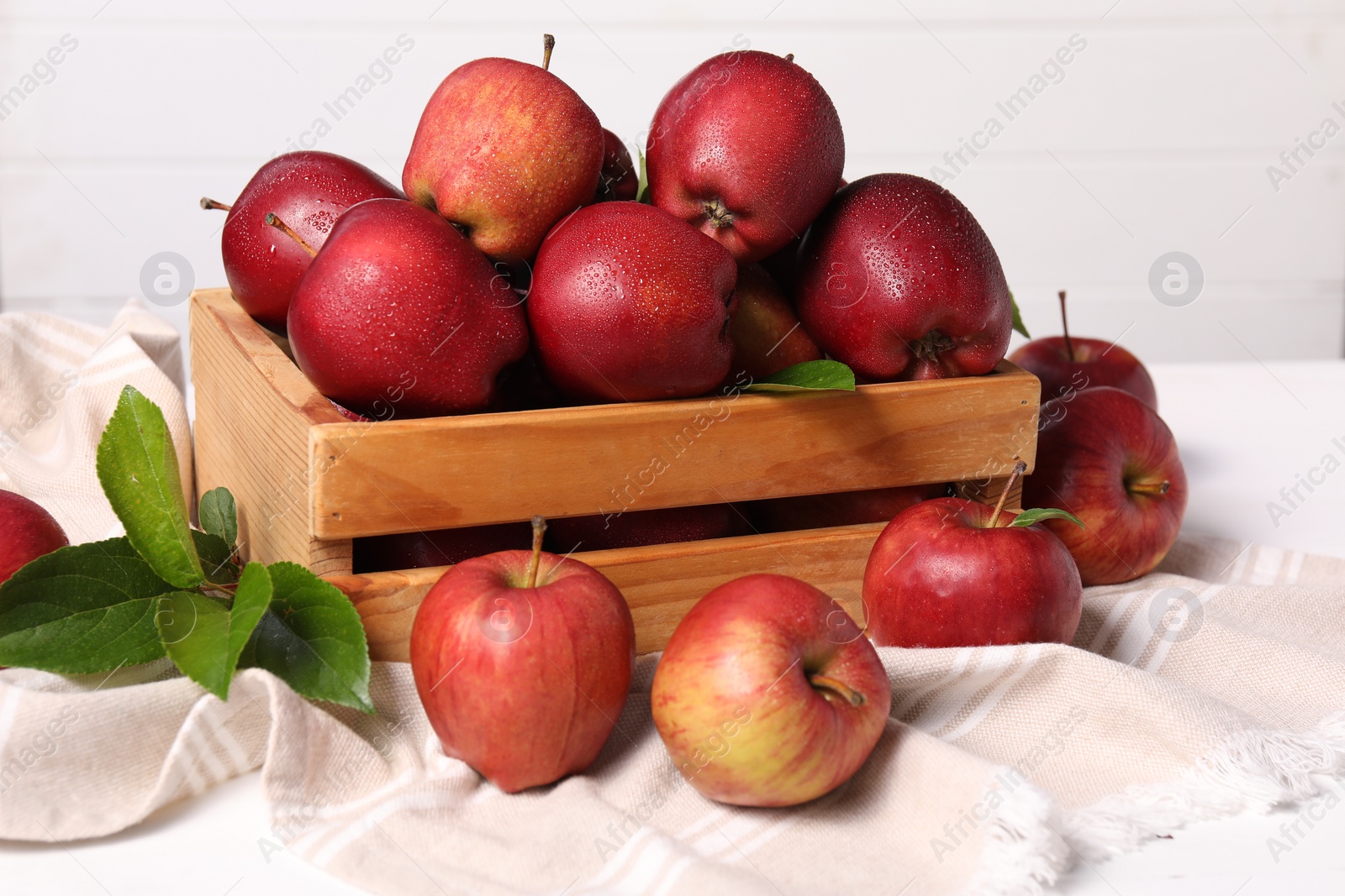 Photo of Fresh red apples and leaves in wooden crate on white table