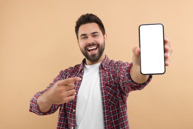 Young man showing smartphone in hand and pointing at it on beige background