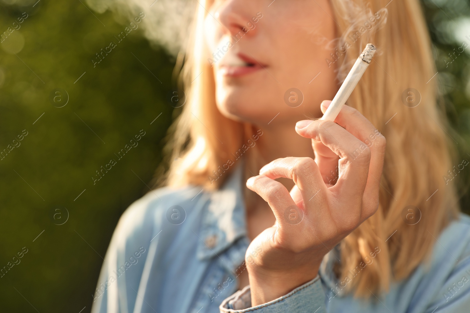 Photo of Young woman smoking cigarette outdoors, closeup view