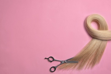 Photo of Lock of blond hair and scissors on color background, top view. Space for text