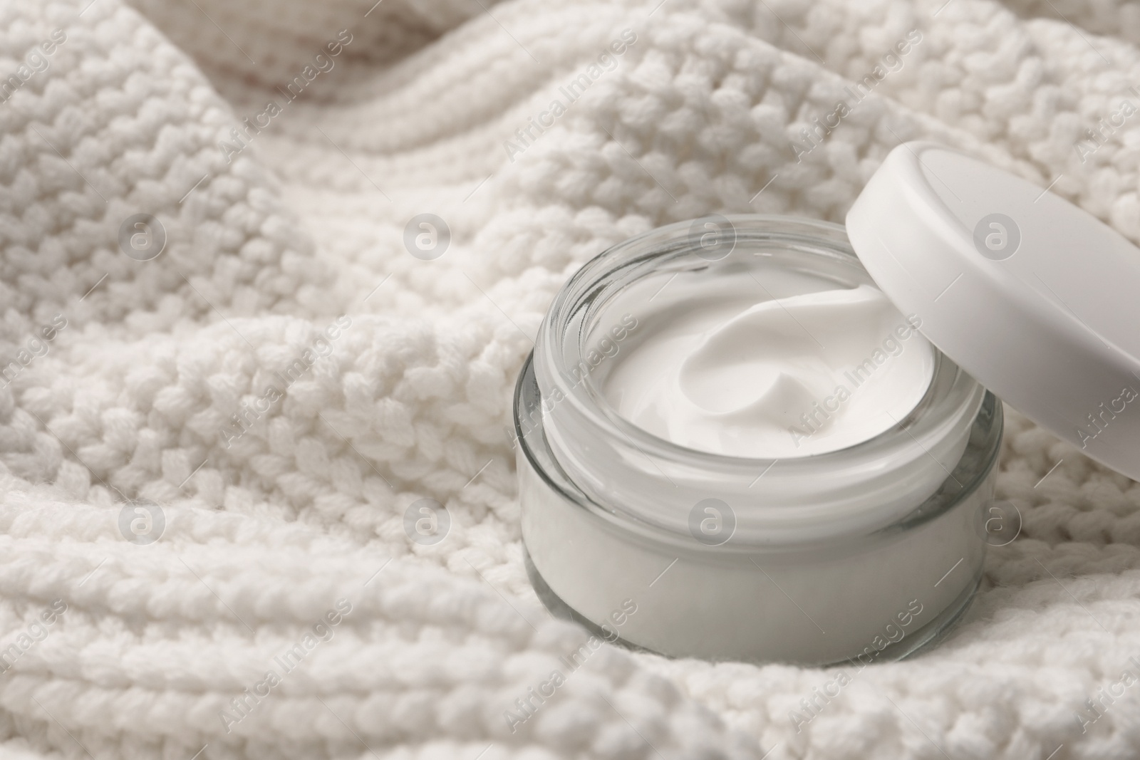 Photo of Winter skin care. Hand cream on white knitted cloth, closeup. Space for text