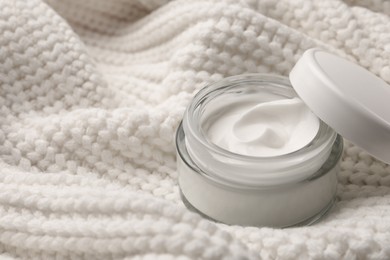 Photo of Winter skin care. Hand cream on white knitted cloth, closeup. Space for text