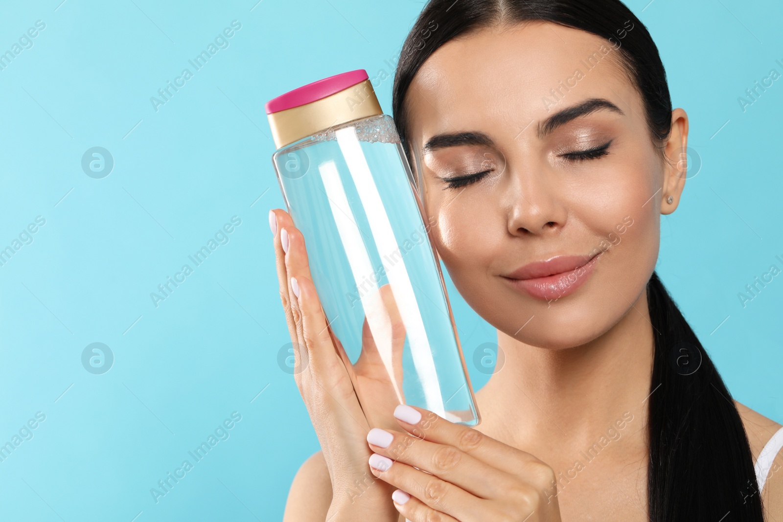 Photo of Young woman with bottle of micellar water on light blue background, space for text