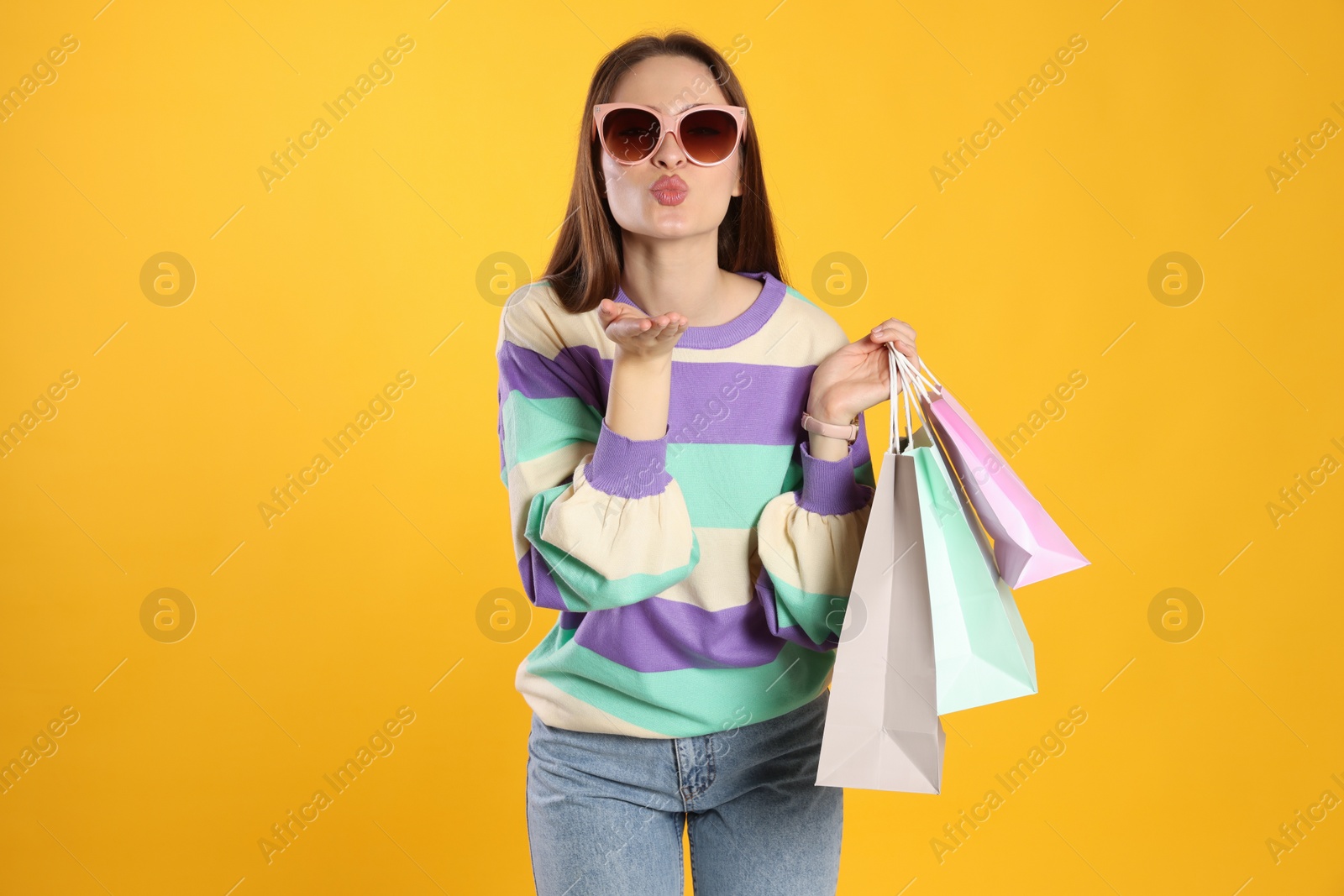 Photo of Beautiful young woman with shopping bags on yellow background. Big sale