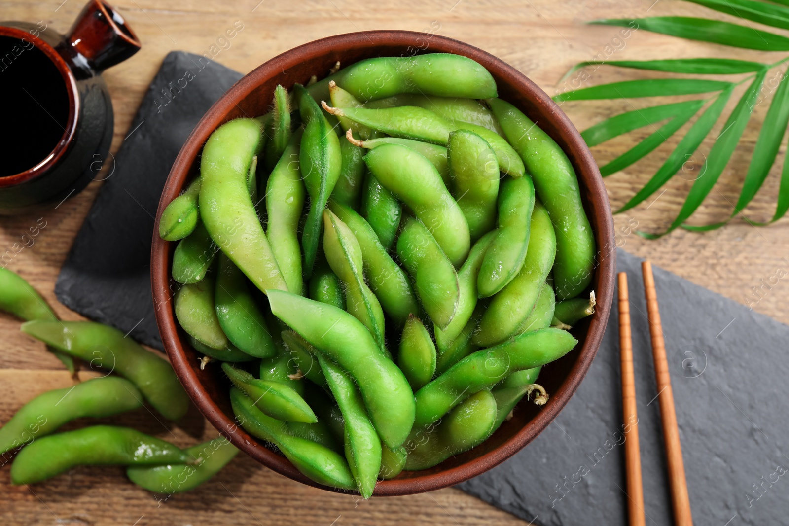 Photo of Green edamame beans in pods served with soy sauce on wooden table, flat lay