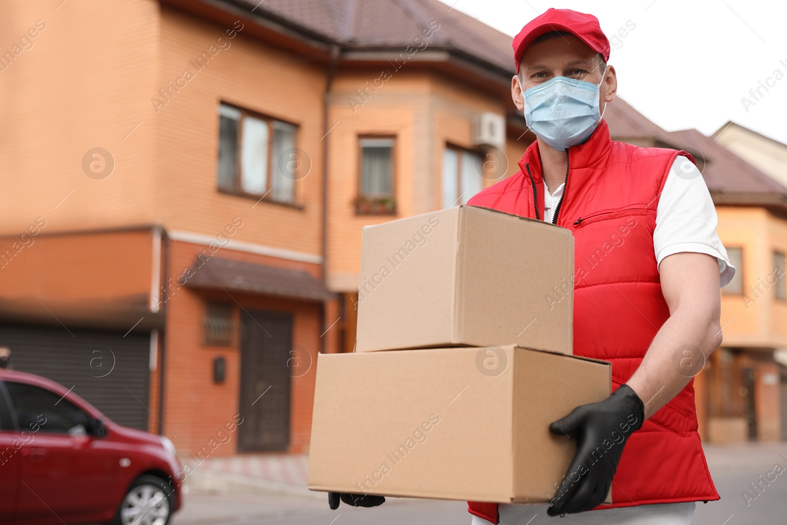 Photo of Courier in protective mask and gloves with boxes near house outdoors. Delivery service during coronavirus quarantine