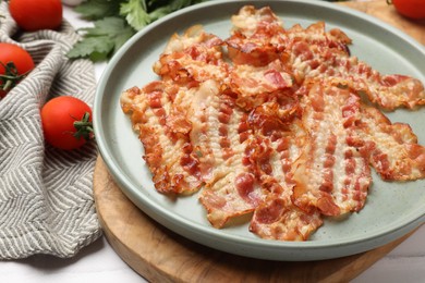 Delicious fried bacon slices and other products on white wooden table, closeup