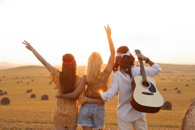 Photo of Hippie friends with guitar showing peace signs in field, back view
