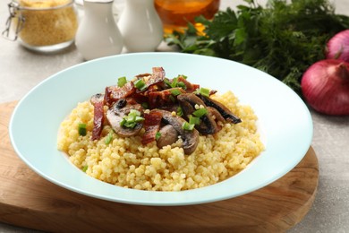 Photo of Tasty millet porridge with mushrooms, bacon and green onion on grey table, closeup