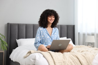 Photo of Beautiful young woman in stylish pyjama using laptop on bed at home