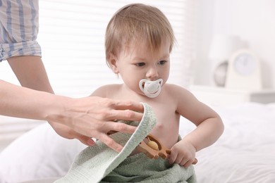 Mother wrapping her cute little baby with towel after bathing on bed