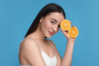 Photo of Beautiful young woman with pieces of orange on light blue background