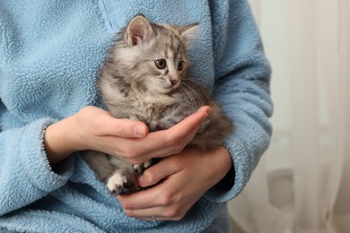 Photo of Woman holding cute fluffy kitten at home, closeup