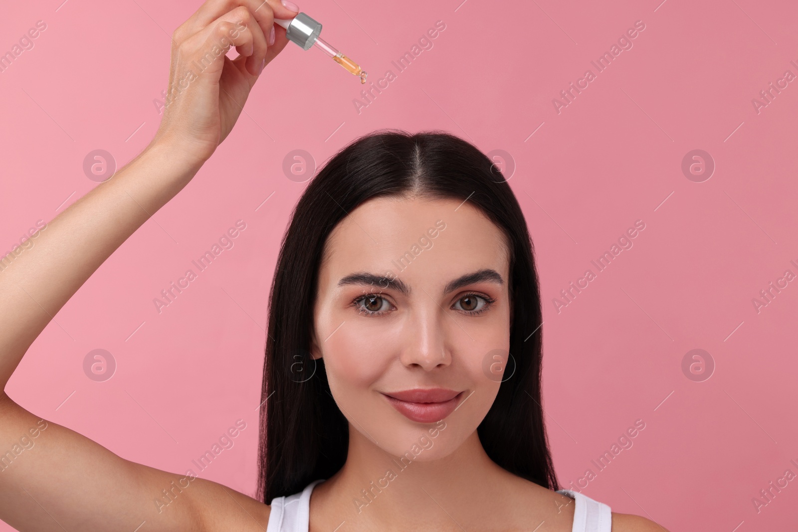 Photo of Beautiful woman applying hair serum on pink background. Cosmetic product