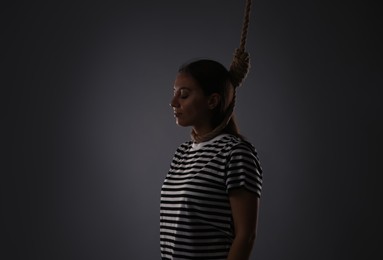 Depressed woman with rope noose on neck against grey background