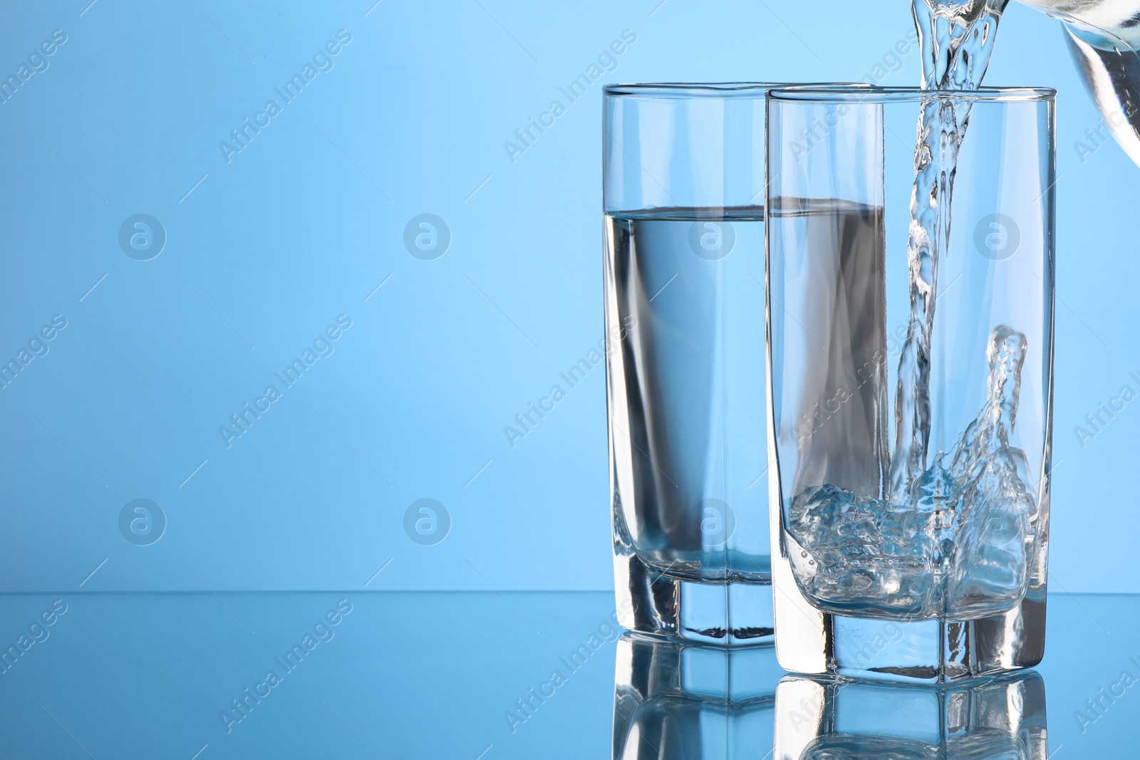 Photo of Pouring water into glass on light blue background. Space for text