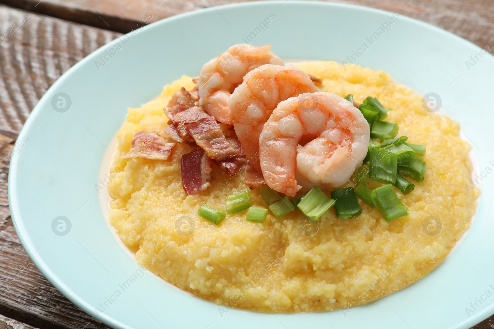 Photo of Plate with fresh tasty shrimps, bacon, grits and green onion on wooden table, closeup