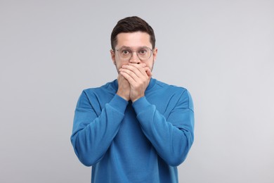 Embarrassed man covering mouth on light grey background