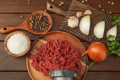 Meat grinder with beef mince, onion, parsley, garlic and spices on wooden table, flat lay