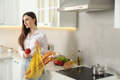 Woman with string bag of baguettes and apple in kitchen