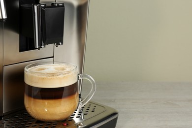 Photo of Modern coffee machine with glass cup of latte on wooden table, closeup. Space for text