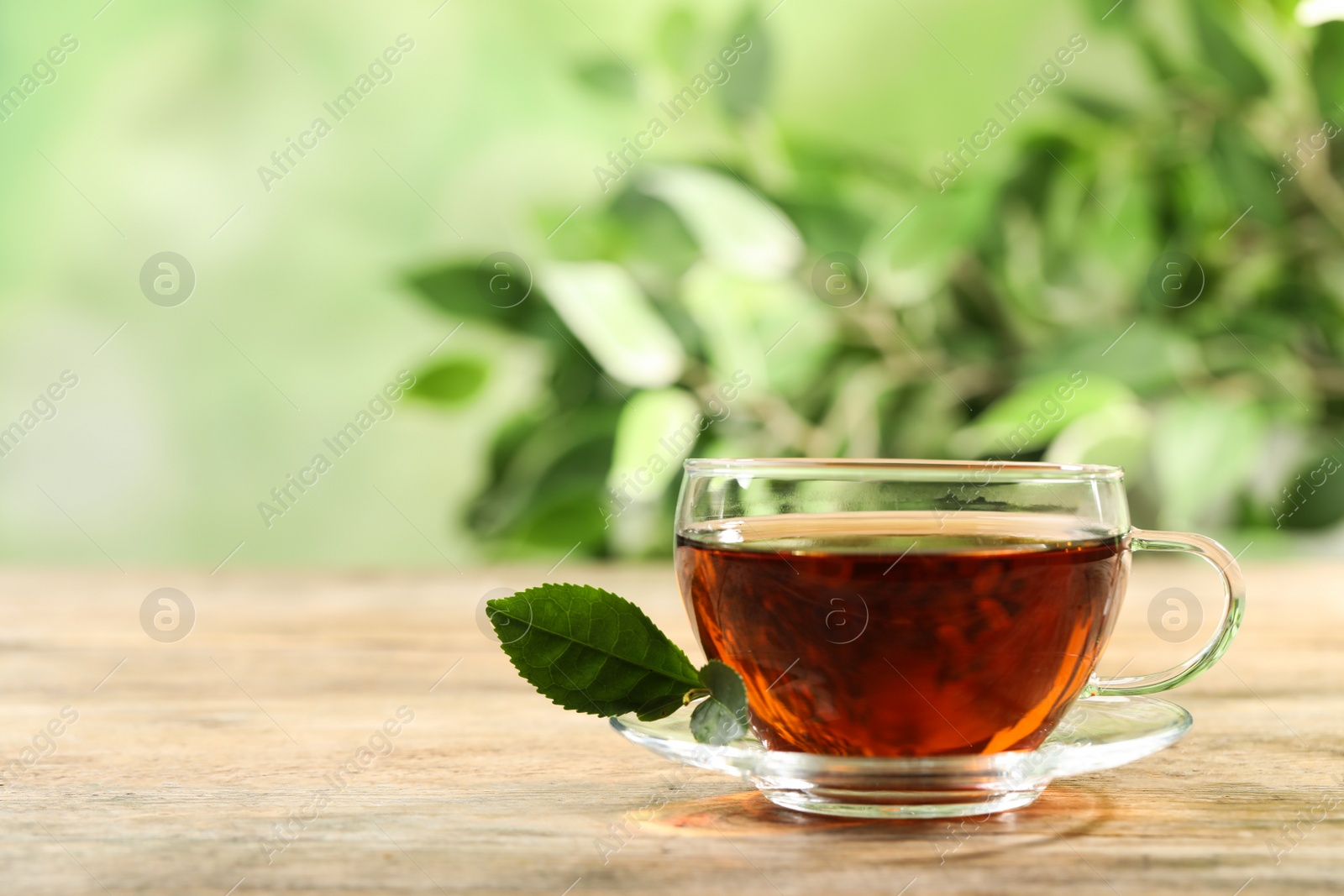 Photo of Cup of black tea on wooden table against blurred background. Space for text