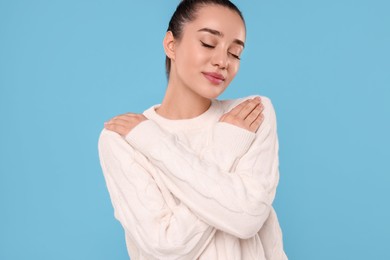 Beautiful young woman in stylish warm sweater on light blue background